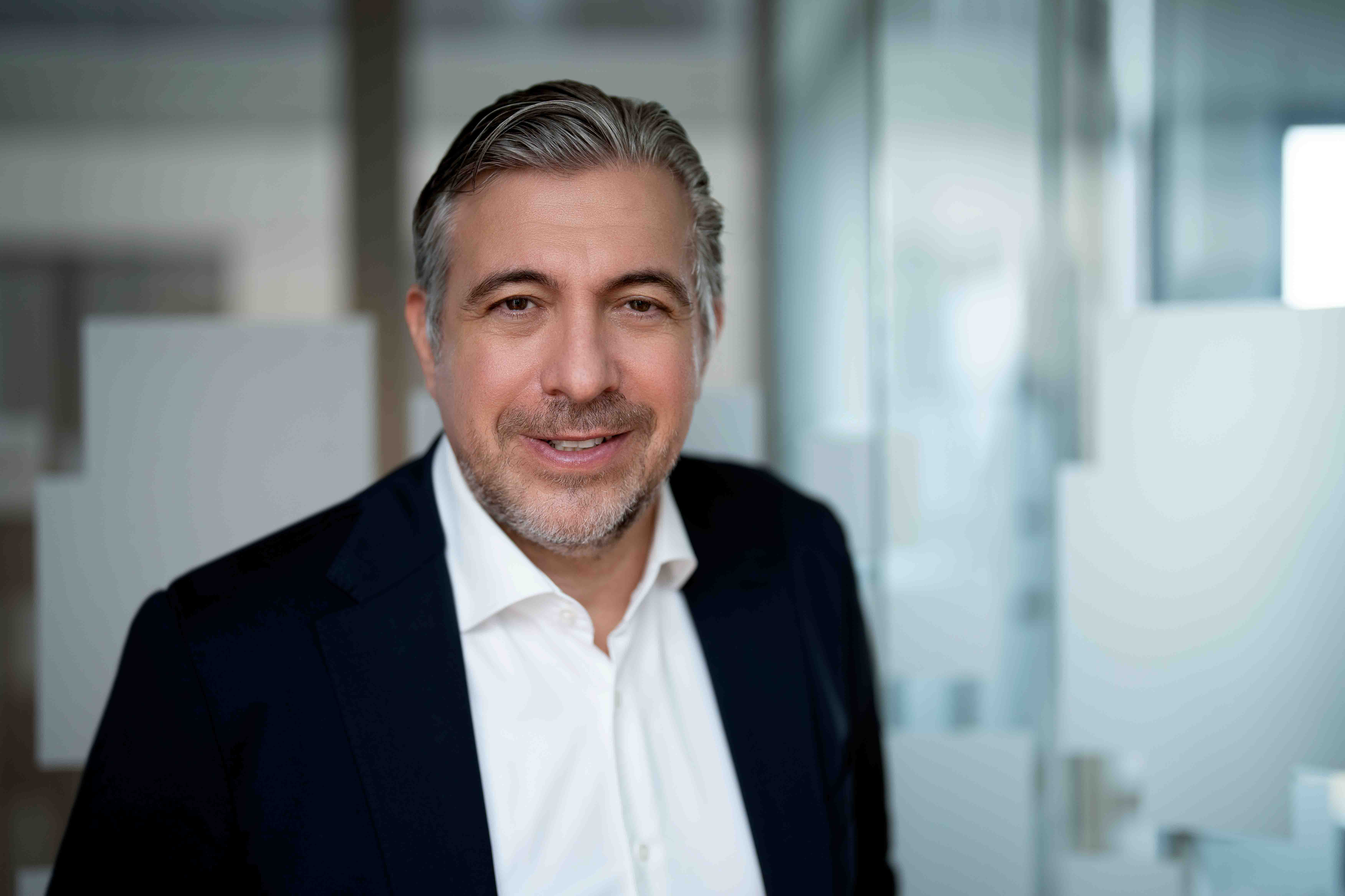 Mann lächelt in Geschäftsanzug, steht in modernem Büro.