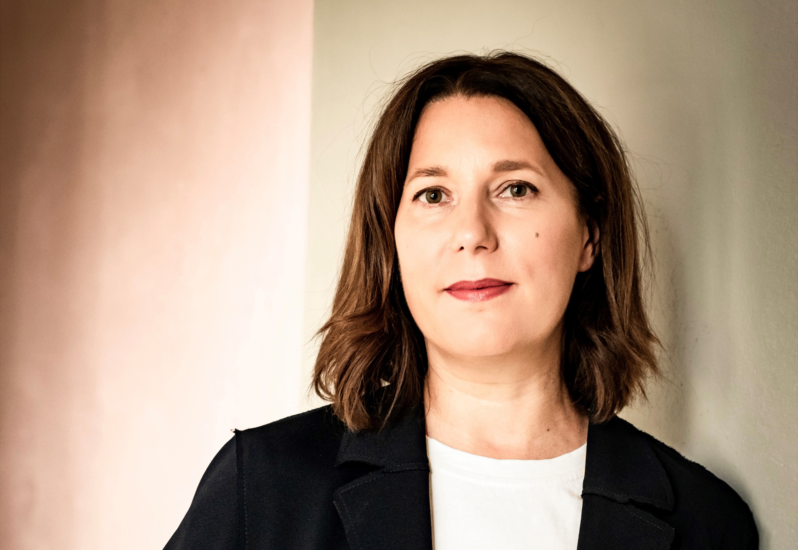 Zu sehen ist eine Frau mit dunklen, schulterlangen haaren, einem schwarzen Blazer und einem weißen Shirt unter dem Blazer.